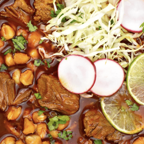 Stew with pork, vegetables in a thick tomato based sauce with slaw, radishes, and limes on top.